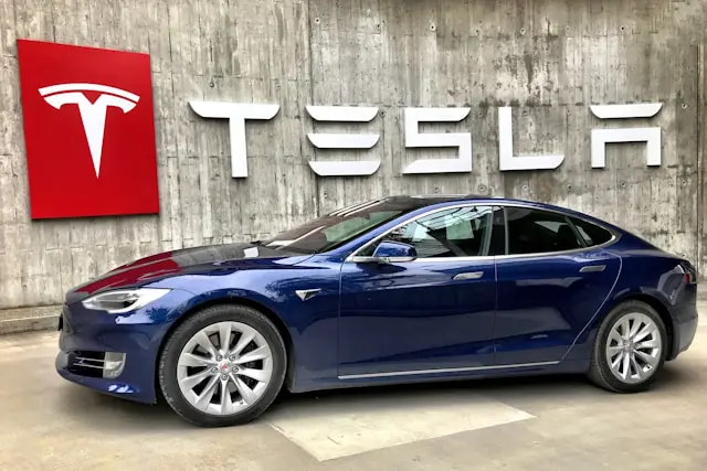 a blue Tesla car in front of a Tesla sign