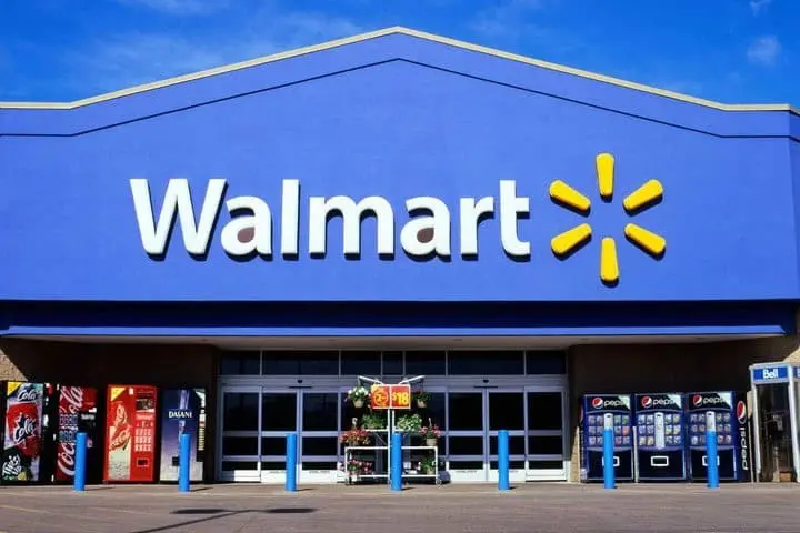 Exterior of a Walmart store with the company logo on a large blue facade, vending machines outside, and clear skies overhead.