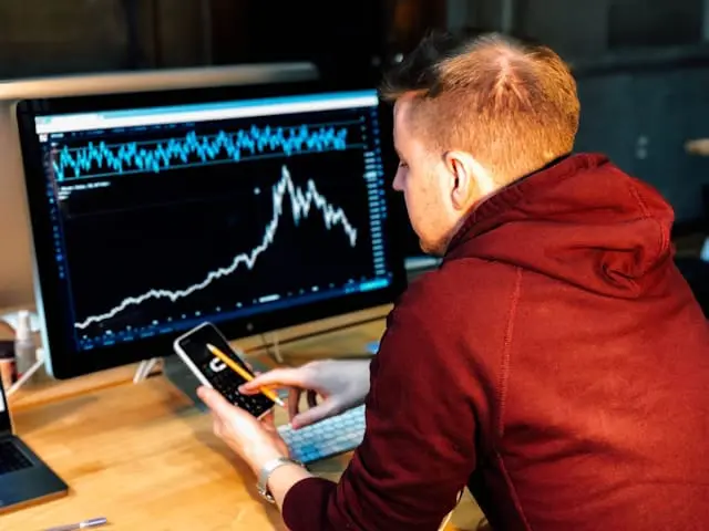 a man holding a phone in front of a monitor 