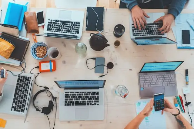 people sitting down at a table with assorted laptop computers