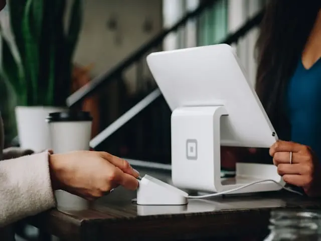 Customer making a payment with a card reader at a modern point-of-sale terminal in a coffee shop setting.