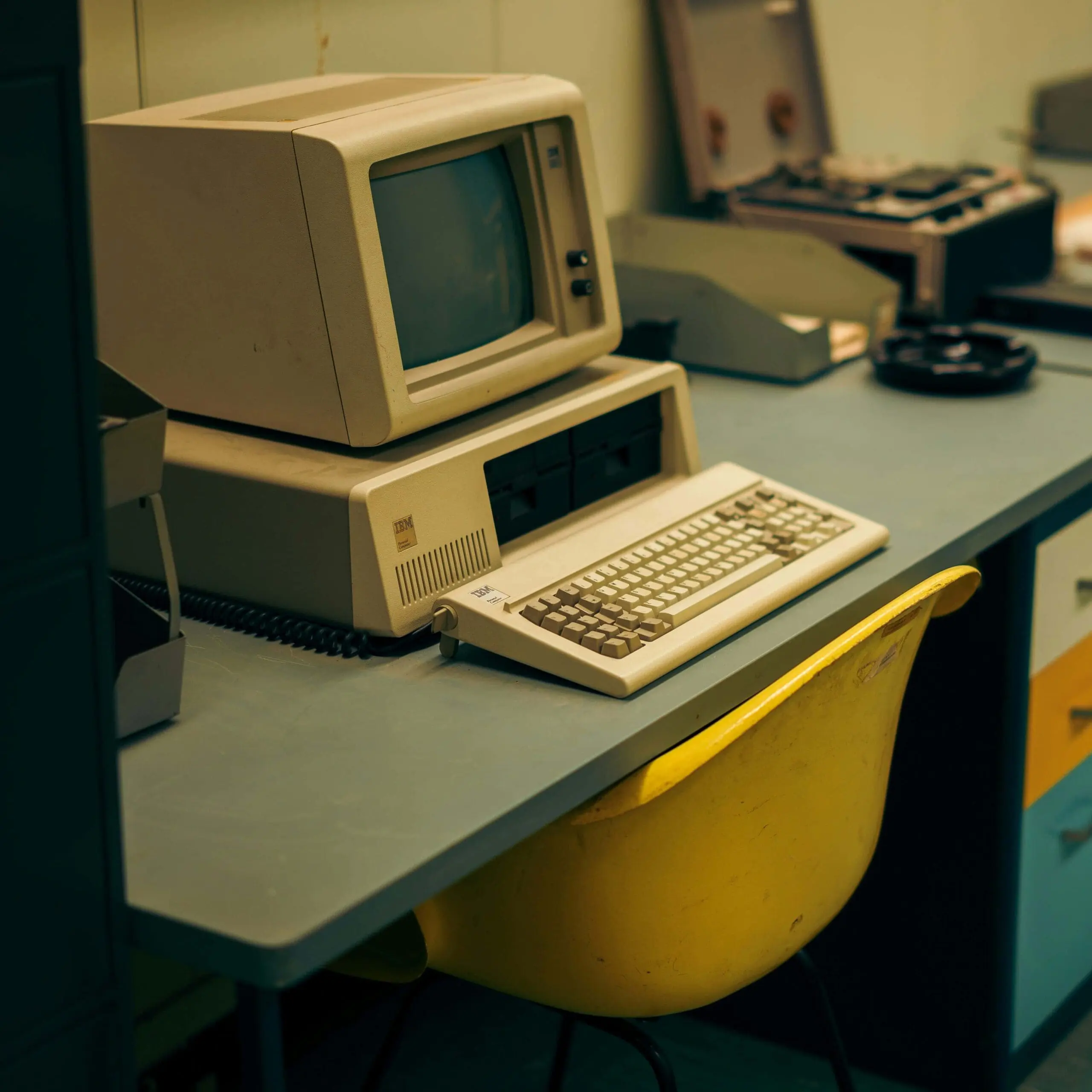 Vintage IBM desktop computer with floppy disk drives on an office desk, symbolizing outdated enterprise technology still in use.