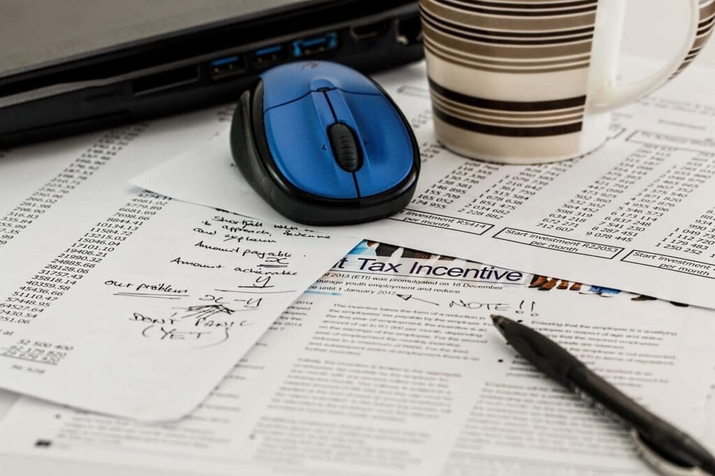 Financial documents with tax incentive form, handwritten notes, a pen, and a blue mouse on a desk.