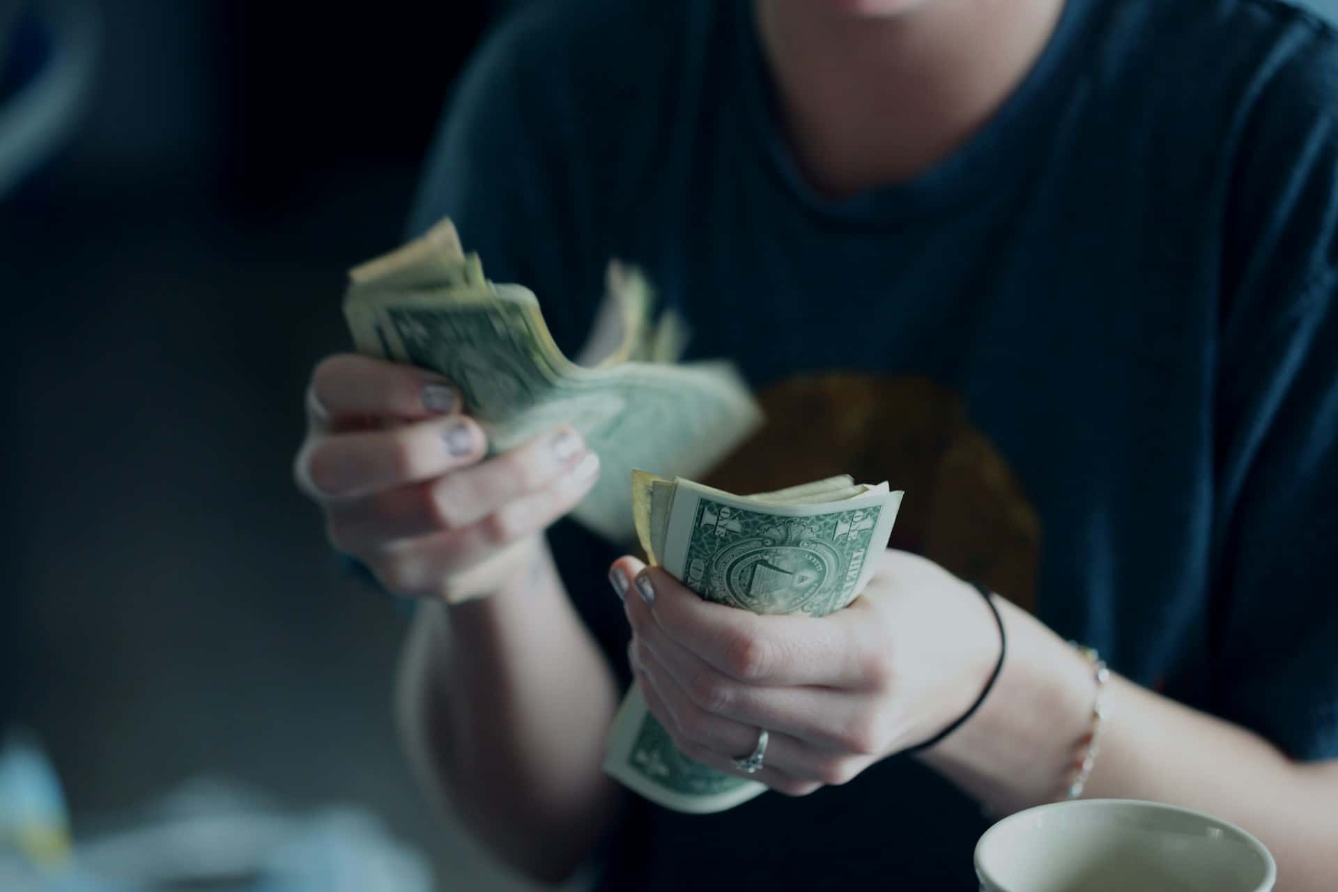 Person counting a stack of U.S. dollar bills, illustrating cash handling or budget planning.