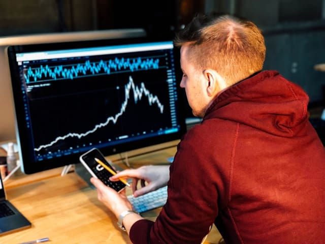 a man holding a phone in front of a monitor 